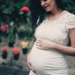 close up photo of pregnant woman in white dress holding her stomach