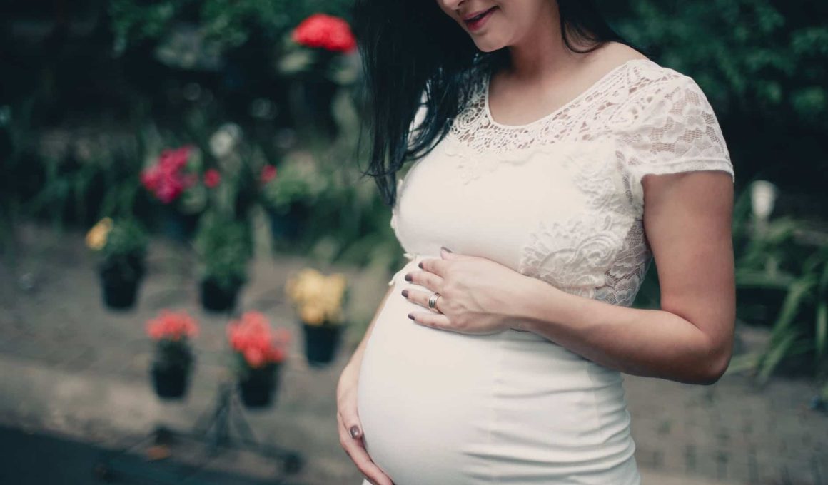 close up photo of pregnant woman in white dress holding her stomach