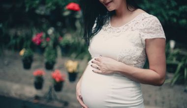 close up photo of pregnant woman in white dress holding her stomach