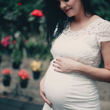 close up photo of pregnant woman in white dress holding her stomach