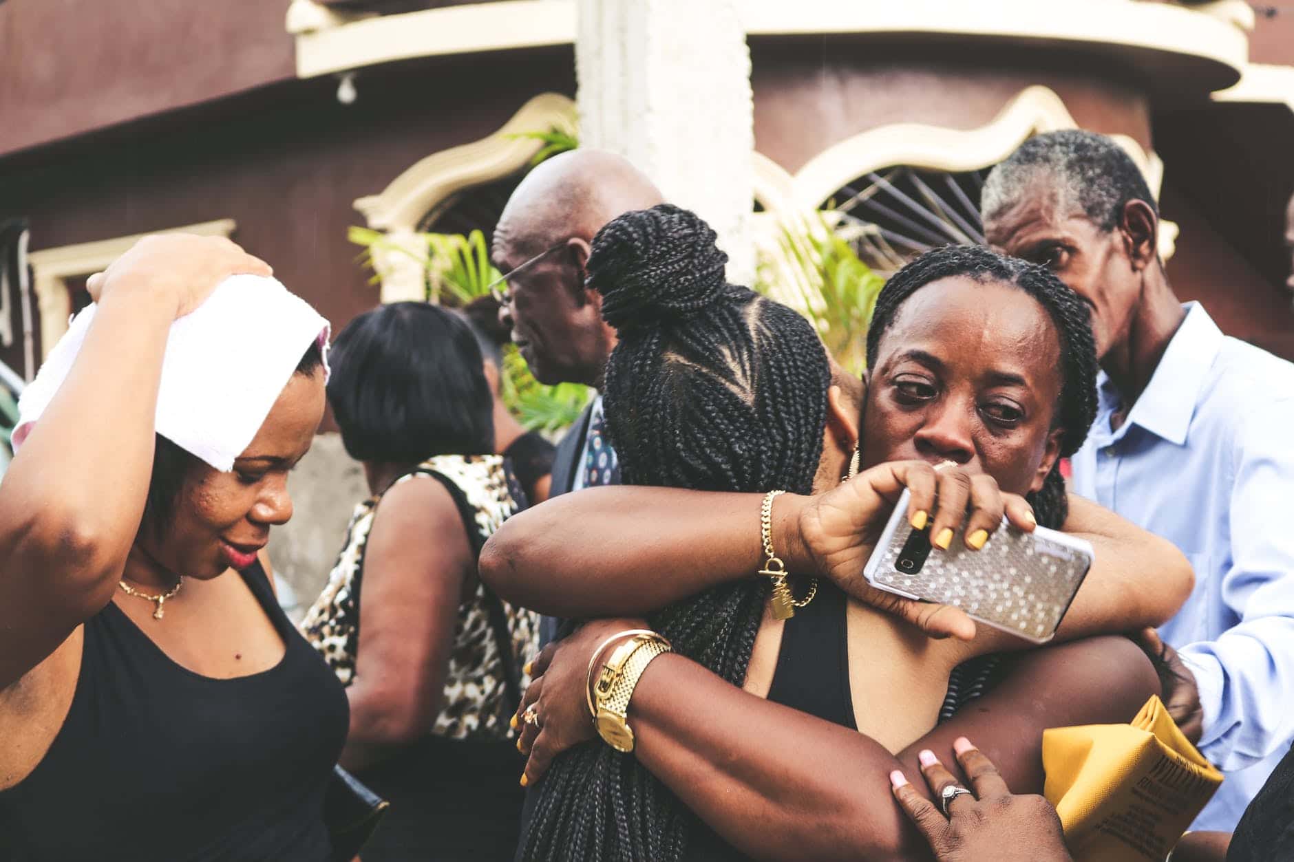 upset black woman embracing anonymous girlfriend near group of people