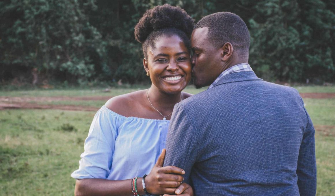 man kissing left cheek of smiling woman