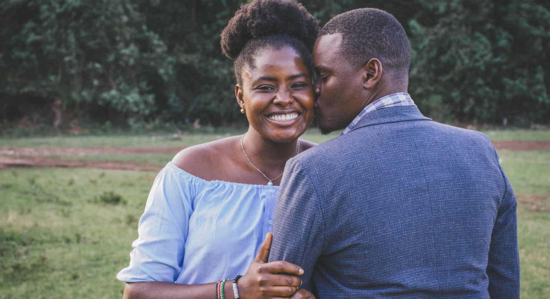 man kissing left cheek of smiling woman