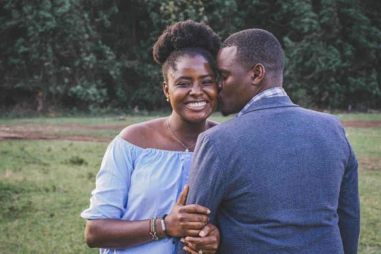 man kissing left cheek of smiling woman