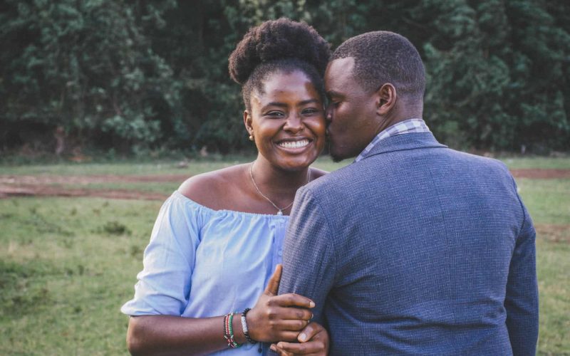 man kissing left cheek of smiling woman