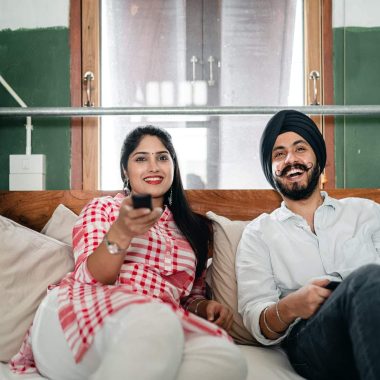 happy young indian couple watching tv in bedroom together