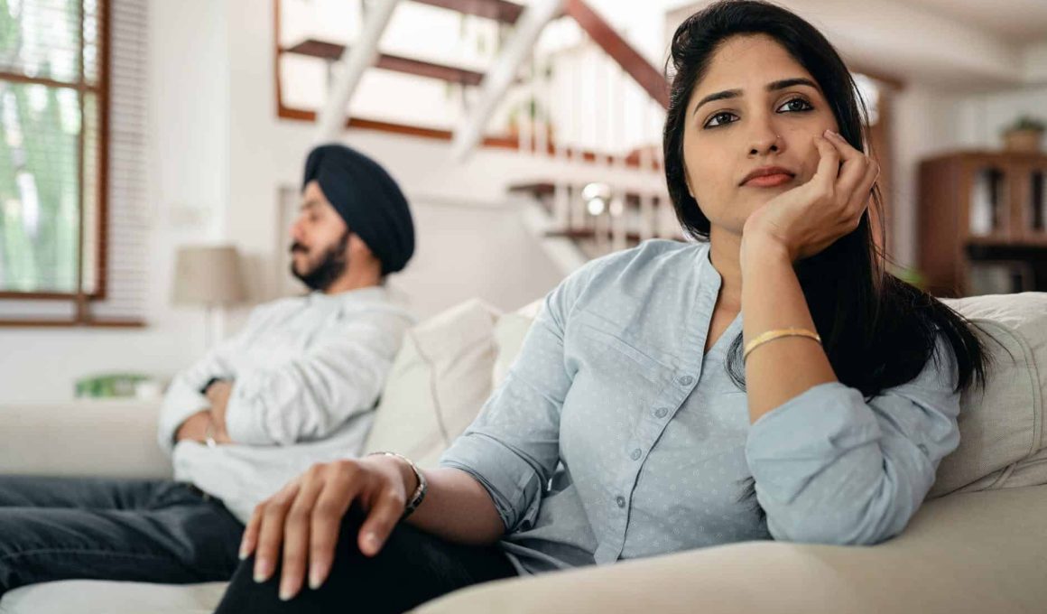 sad young indian woman avoiding talking to husband while sitting on sofa