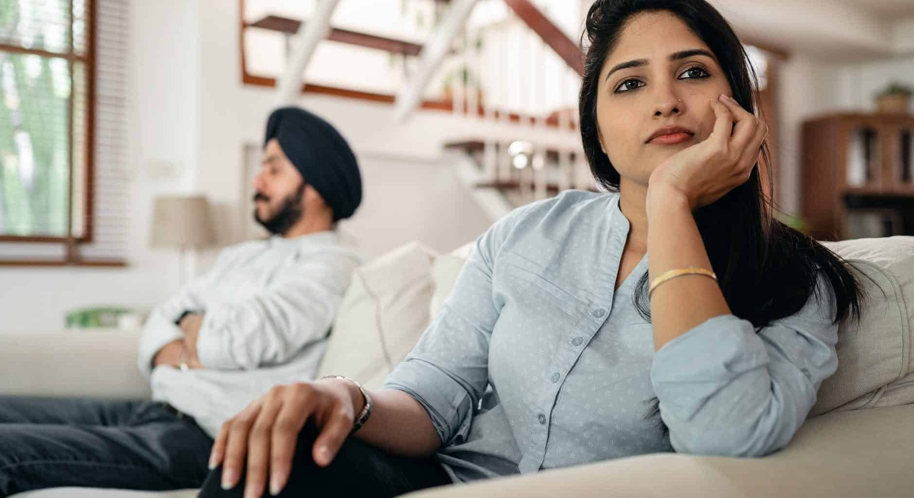 sad young indian woman avoiding talking to husband while sitting on sofa