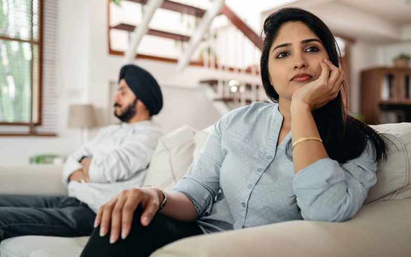 sad young indian woman avoiding talking to husband while sitting on sofa