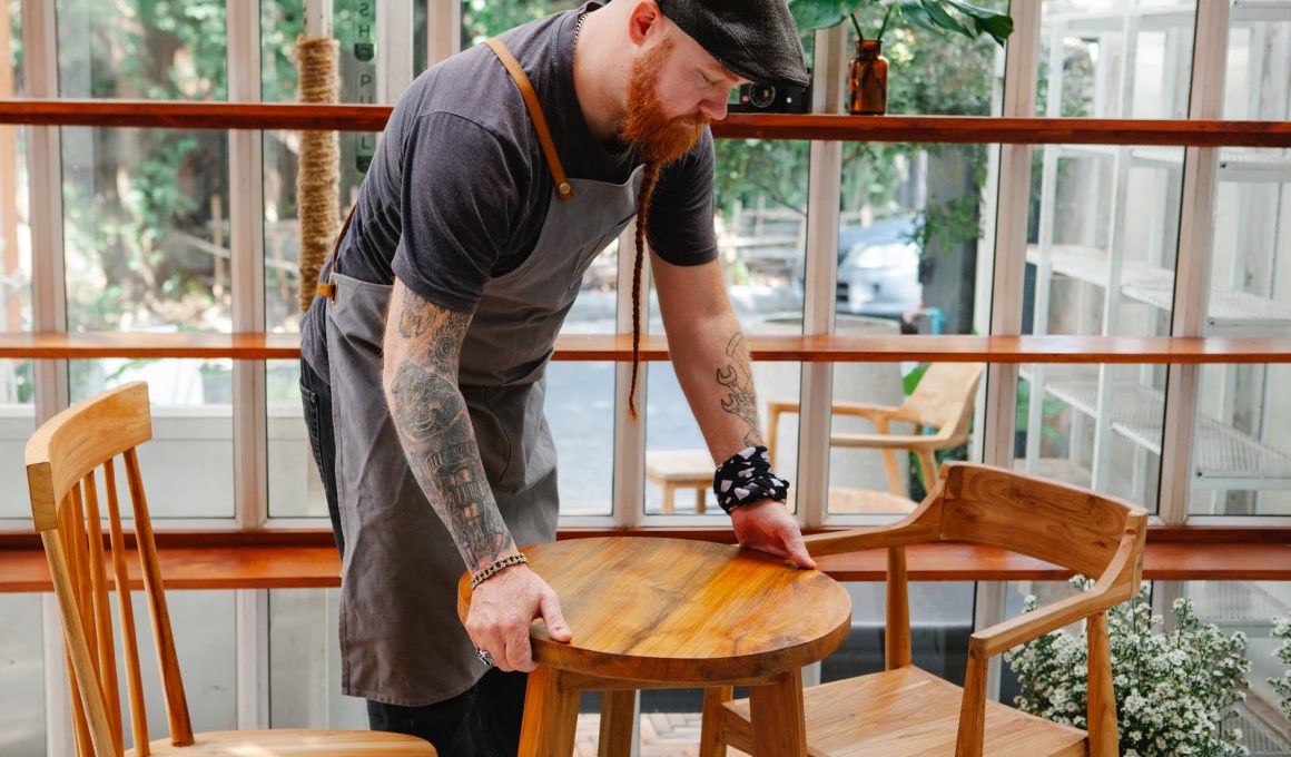 crop cafeteria worker with tattoos putting table on floor