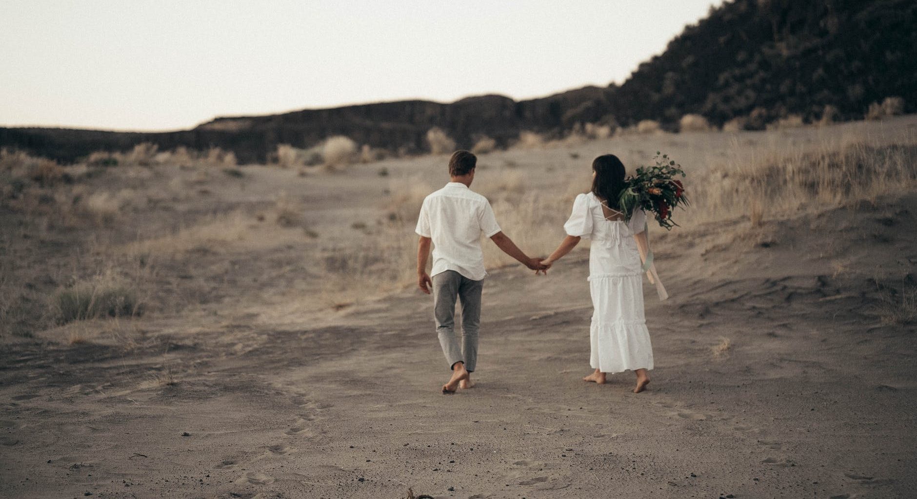 unrecognizable wedding barefoot couple walking on sandy terrain