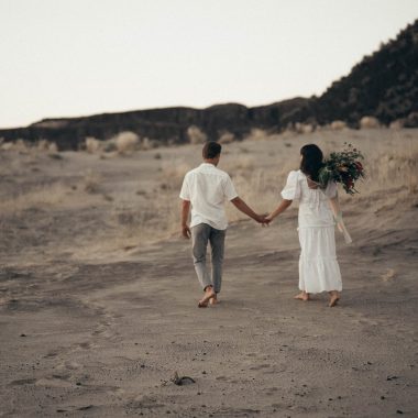 unrecognizable wedding barefoot couple walking on sandy terrain