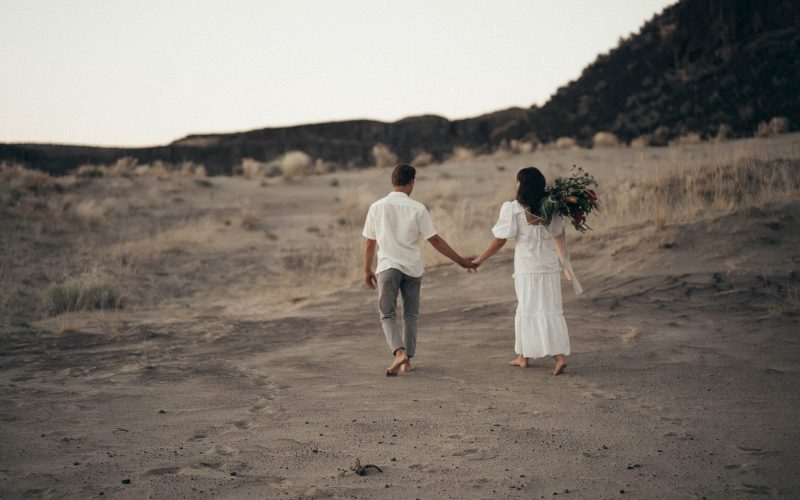 unrecognizable wedding barefoot couple walking on sandy terrain