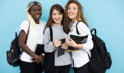 joyful diverse female students standing with books in studio