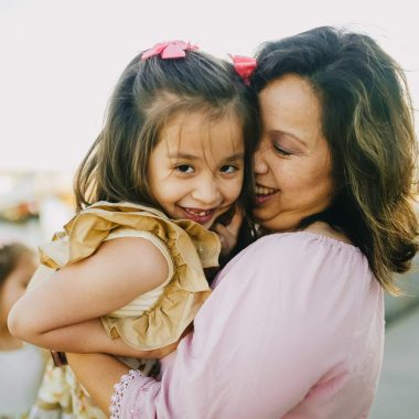 woman in pink long sleeve shirt carrying girl in white and brown floral dress