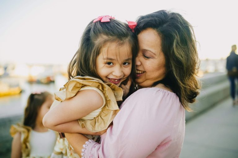 woman in pink long sleeve shirt carrying girl in white and brown floral dress