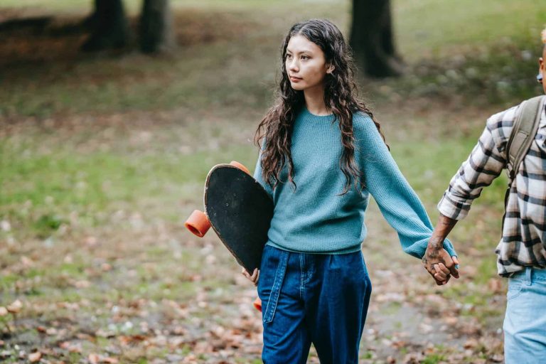 hispanic woman with longboard walking with crop partner