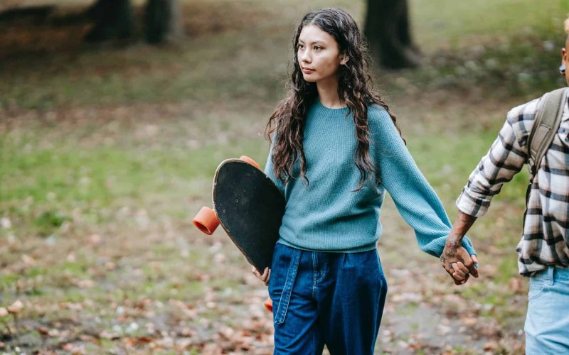 hispanic woman with longboard walking with crop partner