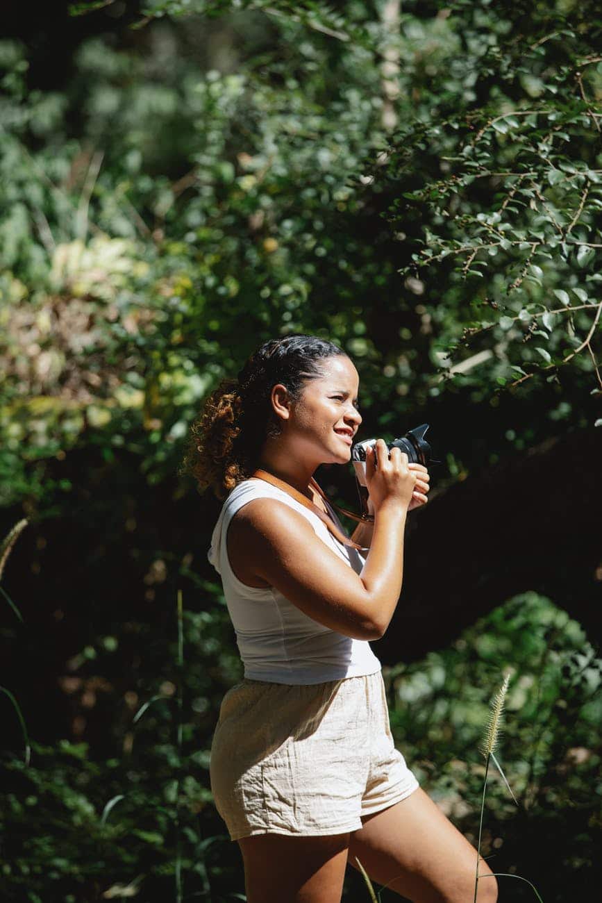 glad ethnic woman with photo camera in woods