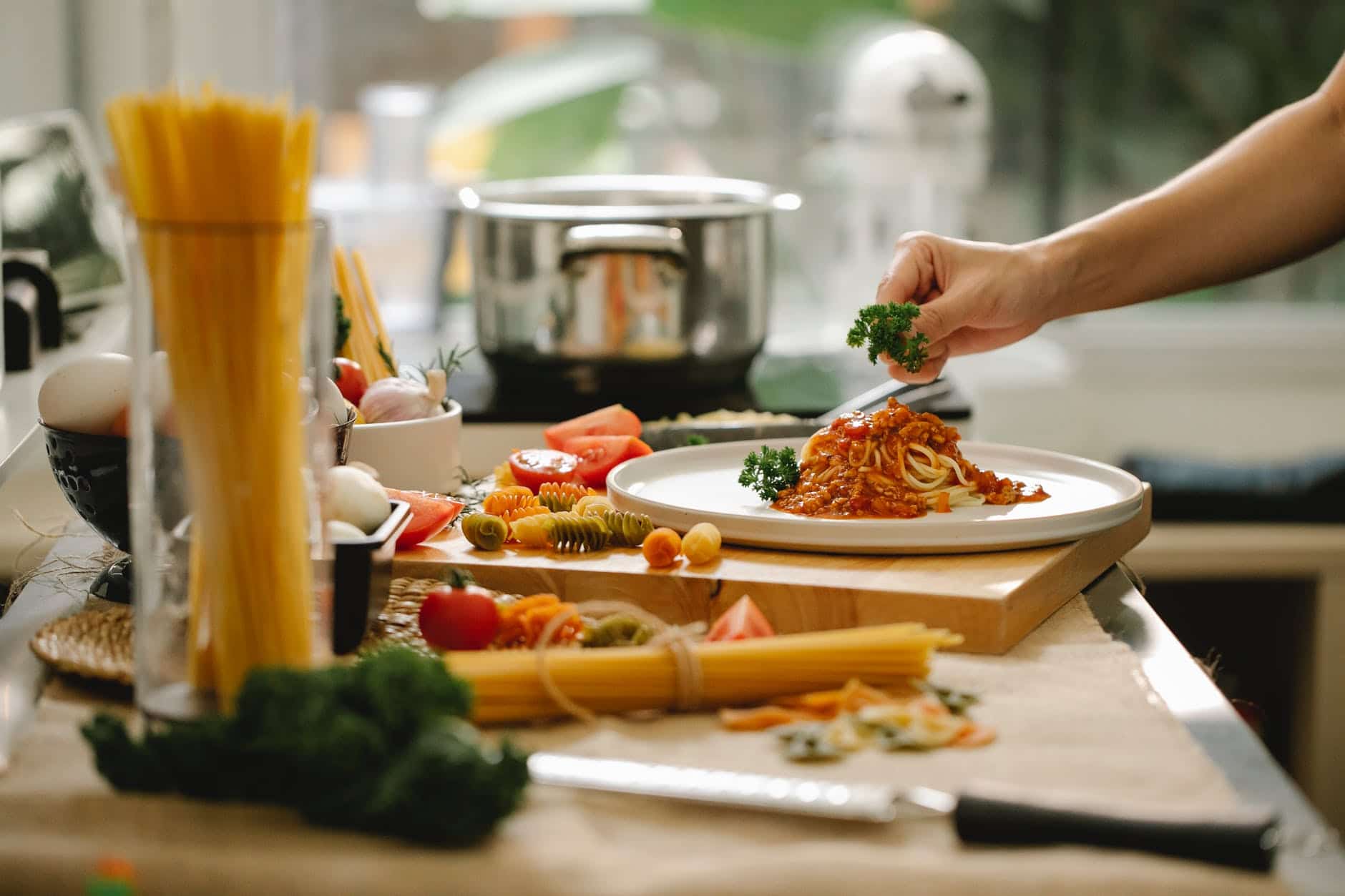 cook adding greens to pasta in kitchen