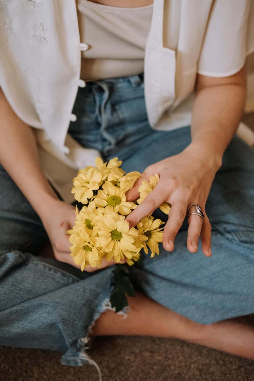 crop faceless woman sitting on floor with bunch of chrysanthemums