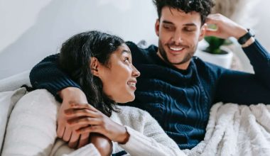 cheerful multiethnic couple resting on couch under blanket
