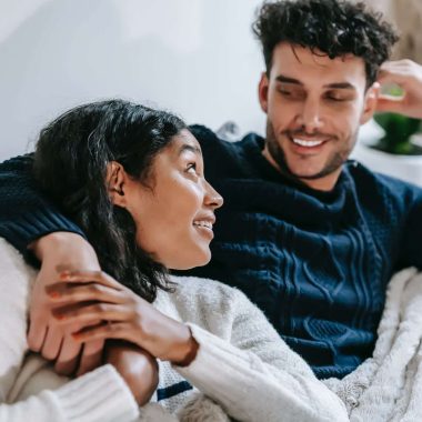 cheerful multiethnic couple resting on couch under blanket