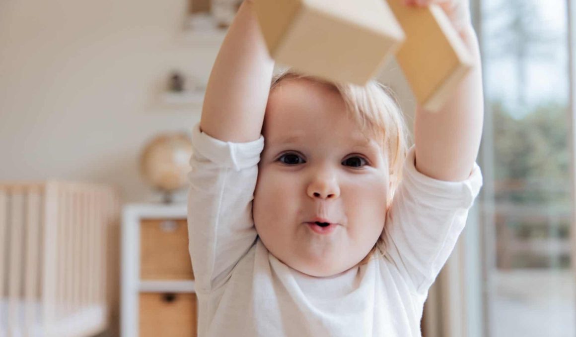 baby in white onesie holding wooden blocks