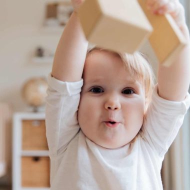 baby in white onesie holding wooden blocks