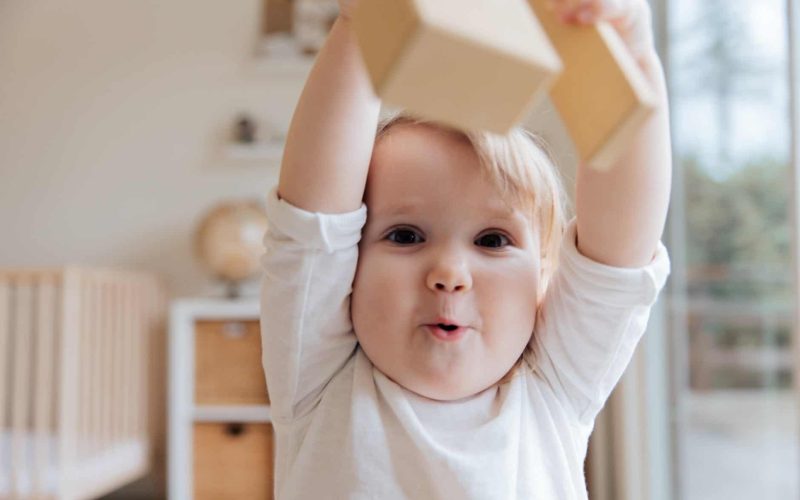 baby in white onesie holding wooden blocks