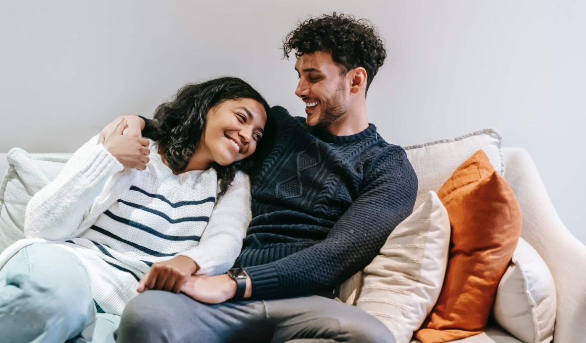 smiling multiracial couple hugging on couch