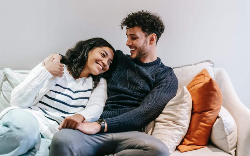 smiling multiracial couple hugging on couch