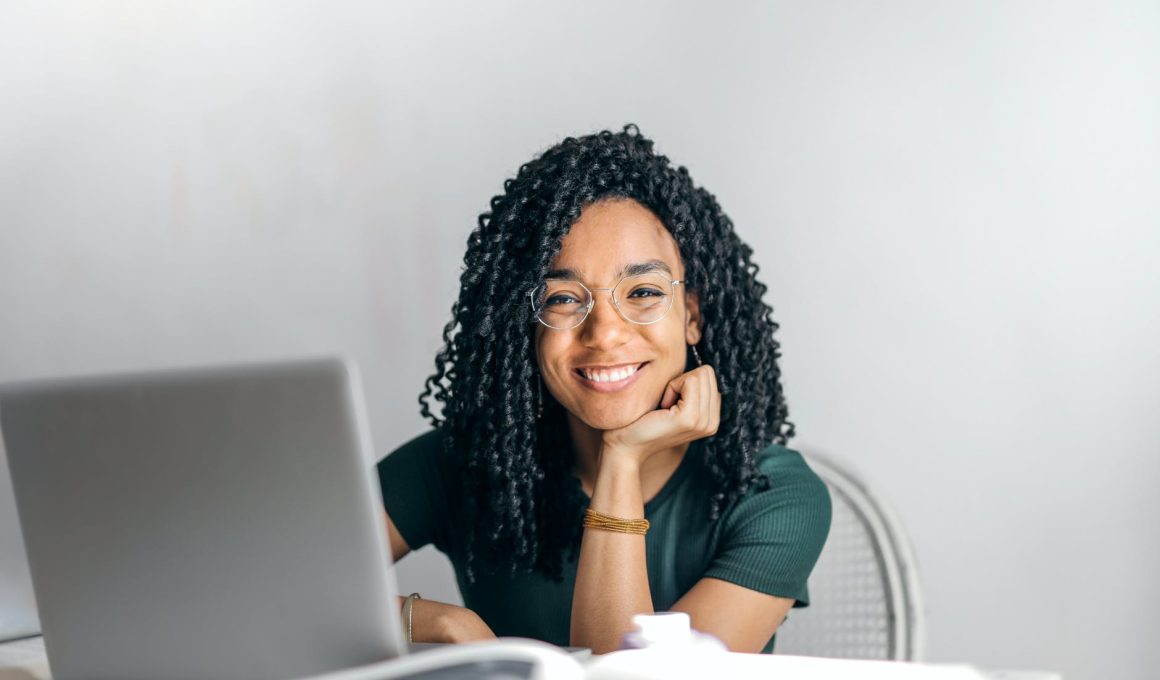 happy ethnic woman sitting at table with laptop